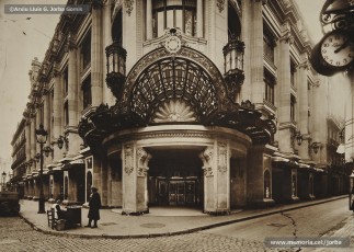 (2/5) Febrer de 1933. Entrada dels Magatzems Jorba de Barcelona. A l’arc de la marquesina que cobreix l’entrada es pot veure un medalló amb el lema de l’empresa “Labor omnia vincit”. El disseny d’aquest emblema, amb els símbols del treball i del comerç, correspon al dibuixant, empleat de l’empresa, Josep Algué, i la frase en llatí està extreta de l’obra Les Geòrgiques, de Virgili.