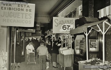 (1/12) Maig de1959. Paradetes amb tot d’ofertes de fira que Magatzems Jorba muntava als porxos que donaven al carrer Nou i al xamfrà de la Plaça de Sant Domènec.