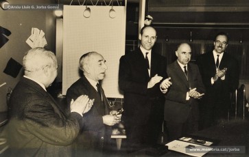 (1/14) Any 1965. Homenatge a Lluis Torra Pujol (1900-1968) amb motiu de la seva jubilació. Aquest empleat havia treballat 50 anys a Can Jorba, a l’administració de la secció de queviures. L’acompanyen Pere Jorba Puigsubirà, a la seva dreta, i Lluís G. Jorba Gomis, a la seva esquerra. Pere Jorba Puigsubirà féu el parlament en nom de l’empresa.