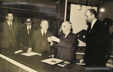(3/14) Any 1965. Homenatge a Lluis Torra Pujol (1900-1968) amb motiu de la seva jubilació. Aquest empleat havia treballat 50 anys a Can Jorba, a l’administració de la secció de queviures. L’acompanyen Pere Jorba Puigsubirà, a la seva dreta, i Lluís G. Jorba Gomis, a la seva esquerra. Pere Jorba Puigsubirà féu el parlament en nom de l’empresa.