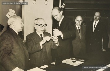 (4/14) Any 1965. Homenatge a Lluis Torra Pujol (1900-1968) amb motiu de la seva jubilació. Aquest empleat havia treballat 50 anys a Can Jorba, a l’administració de la secció de queviures. L’acompanyen Pere Jorba Puigsubirà, a la seva dreta, i Lluís G. Jorba Gomis, a la seva esquerra. Pere Jorba Puigsubirà féu el parlament en nom de l’empresa.