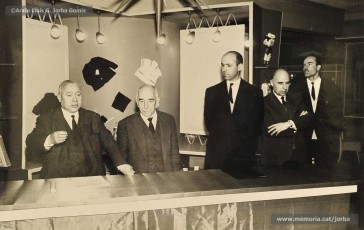 (5/14) Any 1965. Homenatge a Lluis Torra Pujol (1900-1968) amb motiu de la seva jubilació. Aquest empleat havia treballat 50 anys a Can Jorba, a l’administració de la secció de queviures. L’acompanyen Pere Jorba Puigsubirà, a la seva dreta, i Lluís G. Jorba Gomis, a la seva esquerra. Pere Jorba Puigsubirà féu el parlament en nom de l’empresa.