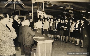 (8/14) Any 1965. Homenatge a Lluis Torra Pujol (1900-1968) amb motiu de la seva jubilació. Aquest empleat havia treballat 50 anys a Can Jorba, a l’administració de la secció de queviures. L’acompanyen Pere Jorba Puigsubirà, a la seva dreta, i Lluís G. Jorba Gomis, a la seva esquerra. Pere Jorba Puigsubirà féu el parlament en nom de l’empresa.