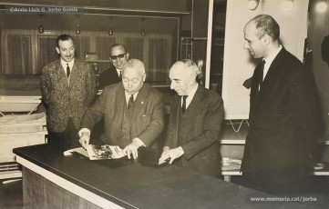 (11/14) Any 1965. Homenatge a Lluis Torra Pujol (1900-1968) amb motiu de la seva jubilació. Aquest empleat havia treballat 50 anys a Can Jorba, a l’administració de la secció de queviures. L’acompanyen Pere Jorba Puigsubirà, a la seva dreta, i Lluís G. Jorba Gomis, a la seva esquerra. Pere Jorba Puigsubirà féu el parlament en nom de l’empresa.