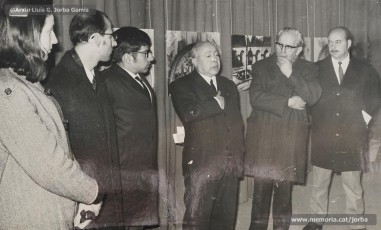 (1/4) 20/2/1969. Presentació de l’exposició d’homenatge a Lluís Uró a càrrec de Pere Jorba Puigsubirà. A la seva esquerra, hi ha el dibuixant Joan Vilanova i, a la seva dreta, el músic Josep Padró i Antoni Fernàndez. L’exposició es feia a la 5ª planta de Cal Jorba.