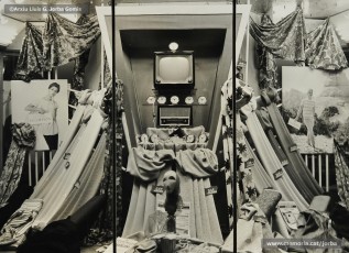 (1/2) Fira de l’Ascensió de 1959. Aparador amb tot de teles i els premis d’un sorteig entre la clientela: un televisor, un aparell de ràdio i nou despertadors; i aparador amb vestits de la primera comunió per a nena.