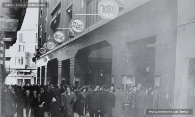 (3/11) 15/2/1959. A l’any 1959 s’havien inaugurat els estudis de Miramar, a Barcelona, cosa que permetia la recepció de les emissions de televisió a Catalunya. Podem veure una multitud de persones que estan mirant encuriosides els aparadors de Cal Jorba per veure el partit entre el Reial Madrid i el FC Barcelona. Magatzems Jorba feia un sorteig de 13 premis, el primer dels quals era un aparell de televisió, entre els seus clients. Els aparells de televisió eren un producte de gran luxe (valien unes 30.000 ptes., el que cobrava un mestre en un any i mig de treball) que poques famílies es podien permetre adquirir.