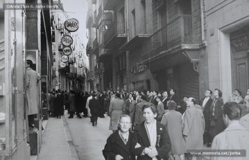 (4/11) 15/2/1959. A l’any 1959 s’havien inaugurat els estudis de Miramar, a Barcelona, cosa que permetia la recepció de les emissions de televisió a Catalunya. Podem veure una multitud de persones que estan mirant encuriosides els aparadors de Cal Jorba per veure el partit entre el Reial Madrid i el FC Barcelona. Magatzems Jorba feia un sorteig de 13 premis, el primer dels quals era un aparell de televisió, entre els seus clients. Els aparells de televisió eren un producte de gran luxe (valien unes 30.000 ptes., el que cobrava un mestre en un any i mig de treball) que poques famílies es podien permetre adquirir.