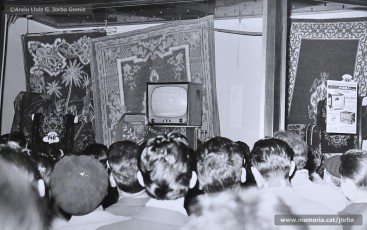 (9/11) 15/2/1959. A l’any 1959 s’havien inaugurat els estudis de Miramar, a Barcelona, cosa que permetia la recepció de les emissions de televisió a Catalunya. Podem veure una multitud de persones que estan mirant encuriosides els aparadors de Cal Jorba per veure el partit entre el Reial Madrid i el FC Barcelona. Magatzems Jorba feia un sorteig de 13 premis, el primer dels quals era un aparell de televisió, entre els seus clients. Els aparells de televisió eren un producte de gran luxe (valien unes 30.000 ptes., el que cobrava un mestre en un any i mig de treball) que poques famílies es podien permetre adquirir.