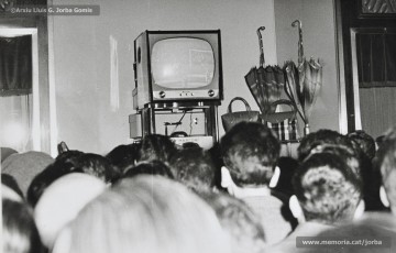 (11/11) 15/2/1959. A l’any 1959 s’havien inaugurat els estudis de Miramar, a Barcelona, cosa que permetia la recepció de les emissions de televisió a Catalunya. Podem veure una multitud de persones que estan mirant encuriosides els aparadors de Cal Jorba per veure el partit entre el Reial Madrid i el FC Barcelona. Magatzems Jorba feia un sorteig de 13 premis, el primer dels quals era un aparell de televisió, entre els seus clients. Els aparells de televisió eren un producte de gran luxe (valien unes 30.000 ptes., el que cobrava un mestre en un any i mig de treball) que poques famílies es podien permetre adquirir.