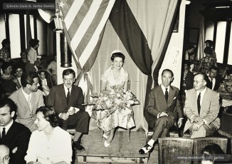 (3/3) 5/6/1960. Miss Cotó asseguda al lloc d’honor de la desfilada entre les banderes d’Espanya i dels Estats Units. A la seva esquerra hi ha Pere Jorba Vall.