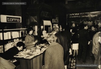 (5/10) Dia del Llibre any 1966. Fira del Llibre organitzada als porxos de Magatzems Jorba com a aportació de l’empresa a la diada de Sant Jordi. S’hi veuen les parades de les llibreries Rubiralta, Torra, Perramon, Escodines, Xipell i Símbol.