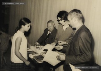 (4/19) Octubre de 1966. Acte de fi de curs 1965-66 de les sessions de cinema infantil. Lliurament del record d’assistència per Pere Jorba Puigsubirà, president del Consell d’Administració de Magatzems Jorba, Dolors Ponsà, empleada de Cal Jorba, i el pare Ferran Torra Sisquella SJ (1893-1990), director de les Congregacions Marianes.