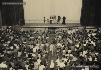 (7/19) Octubre de 1966. Acte de fi de curs 1965-66 de les sessions de cinema infantil. Lliurament del record d’assistència per Pere Jorba Puigsubirà, president del Consell d’Administració de Magatzems Jorba, Dolors Ponsà, empleada de Cal Jorba, i el pare Ferran Torra Sisquella SJ (1893-1990), director de les Congregacions Marianes.