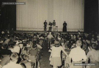 (12/19) Octubre de 1966. Acte de fi de curs 1965-66 de les sessions de cinema infantil. Lliurament del record d’assistència per Pere Jorba Puigsubirà, president del Consell d’Administració de Magatzems Jorba, Dolors Ponsà, empleada de Cal Jorba, i el pare Ferran Torra Sisquella SJ (1893-1990), director de les Congregacions Marianes.