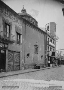 Façana lateral de l'església de Sant Pere Màrtir, vista des del carrer del Born, al començament dels anys vint del segle XX. Al final del carrer, el gran rellotge de la botiga que la casa Jorba havia inaugurat l'any 1893 en un edifici de tres plantes, adossat a l'església.
Procedència: Arxiu Jaume Pons i Agulló.