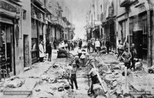 El carrer del Born vist des de la Plana de l'Om en plenes obres de pavimentació l'any 1926. Es poden contemplar alguns establiments antics com la pastisseria L'Englantina o cal Marsinyac, casa fundada l'any 1916, o la carnisseria Fainé, que obrí les seves portes l'any 1911. Per això, al juliol del 1927, Fidel Riu considerava que el carrer del Born «és una síntesi de Manresa: tant en l'ordre social com en l'ordre mercantil», com també «l'eix de Manresa. Es un espai obert al bell mig cor de la ciutat i totes les exaltacions i batecs de la vida manresana hi tenen aculliment».
Procedència: Col·lecció Ramon Salisi i Bonastre.