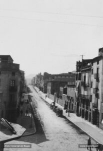 La carretera de Cardona en una fotografia de començaments del segle XX. Juntament amb la carretera de Vic, aquesta fou un dels eixos de creixement urbanístic de la ciutat. Aquest vial experimentà en el decurs del darrer quart de segle un intens procés d'edificació que donà com a resultat la instal·lació de comerços a l'engròs, d'activitats tèxtils i de tallers de diversa índole que treballaven per a les fàbriques de teixits. En aquesta imatge apareix, a tall d'exemple, la fàbrica de Pere Perera, a la dreta.
Procedència: Col·lecció família Soler i Mas