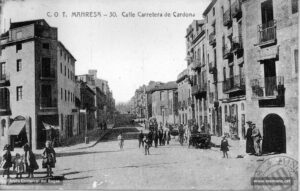 La carretera de Cardona en una fotografia de començaments del segle XX. Juntament amb la carretera de Vic, aquest fou un dels eixos de creixement urbanístic de la ciutat. Aquest vial experimentà en el decurs del darrer quart de segle un intens procés d'edificació que donà com a resultat la instal·lació de comerços a l'engròs, d'activitats tèxtils i de tallers de diversa índole que treballaven per a les fàbriques de teixits. En aquesta imatge apareix, a tall d'exemple, la fàbrica de Pere Perera, a la dreta.
Procedència: Arxiu Comarcal del Bages