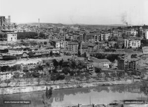 Aspecte del vessant meridional de la ciutat a principis del segle XX, entre l'estació del Nord i el Pont Vell. Des d'aquest indret es poden contemplar la renglera de fàbriques que aprofitaven les escorrialles del torrent de Sant Ignasi, un lloc d'incipient localització industrial. Prop de la capella de Sant Marc se situava la fàbrica de cintes Portabella; més amunt, la històrica fàbrica del Salt (construïda l'any 1862 per l'industrial Josep Pons i Enrich), accionada en un principi per l'energia hidràulica extreta del salt dels Gossos i a partir del 1882 per la força del vapor. Precisament en aquesta data se n'aixecà la xemeneia. Al mig de la fotografia, s'hi pot percebre la desapareguda església de Sant Ignasi. 
Procedència: Col·lecció Ramon Cornet i Arboix. (Fotografia de Lluís Cornet i Vivar)