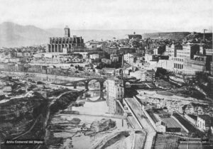 Vista general de Manresa al tombant de segle. L'arbreda del camí de Sant Pau, la fàbrica del Pont Vell i la Cova a la riba dreta del riu; a la riba esquerra, les diverses vies del ferrocarril del Nord. La basílica de la Seu al fons, encimbellada damunt del turó del Puigcardener. 
Procedència: Arxiu Comarcal del Bages