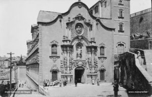 Perspectiva del pòrtic de l'església de la Cova de Sant Ignasi. L'església fou construïda entre els anys 1750 i 1763, però no fou beneïda fins el 1844. L'edifici pertany a l'estil de l'arquitectura anomenada jesuítica. La façana principal que apareix en aquestes imatges és, però, d'inspiració plenament barroca. 
Procedència: Arxiu Jaume Pons i Agulló.
