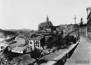 La ciutat vista des de la baixada de la Cova de Sant Ignasi. Imatge obtinguda, molt probablement, al començament dels anys vint del segle passat. Notables millores urbanístiques i arquitectòniques separen aquesta perpectiva de l'anterior: les transformacions de la Seu, l'embelliment del seu parc o antic fossar; l'accés directe a la Casa d'Exercicis (encara per construir en aquesta fotografia); fins i tot, la casa que apareix al peu del camí de la Cova ha sofert obres de reforma i, finalment, cal remarcar que l'electricitat ha arribat també al tantes vegades abandonat districte cinquè (que comprenia el barri de la Cova, torrent de Sant Ignasi, les Escodines i Santa Clara enllà). 
Procedència: Arxiu Comarcal del Bages