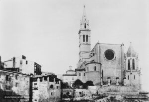 Instantània de la basílica de la Seu tal com era visible des de la plaça de la Reforma vers la meitat dels anys vint. Cal observar que el nou pòrtic de la façana principal encara no ha estat construït, però sí que s'havia remodelat el campanar i s'havia aixecat el nou baptisteri. Al peu de la torre-campanar, es pot veure la capella dels favets o de la Puríssima. 
Procedència: Arxiu Jaume Pons i Agulló