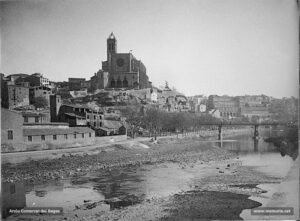 Panoràmica del sector de la Reforma pels volts del 1910. El passeig del Riu, flanquejat pels plàtans inconfusibles. Totes les cases existents al redós del portal de les Piques ja no hi són. Al gener del 1879 s'aprovà el projecte d'ampliació de la plaça d'en Creus, i un mes més tard es començaven a enderrocar les cases del portal de les Piques. En efecte, la zona que coneixem com la Reforma començà a ser condicionada per fases, i de manera molt lenta, el darrer quart del segle XIX, i culminà amb la finalització de l'obertura del carrer d'Alfons XII, inaugurat l'any 1970. La basílica de la Seu encara no ha sofert les reformes a la façana de ponent, i tampoc no s'hi ha construït l'escalinata, ni remodelat el campanar. 
Procedència: Jaume Pons i Agulló.