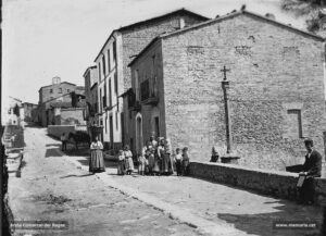 Esplèndida vista de la creu vella del Tort al carrer Nou de Santa Clara. Al fons, el monestir que dóna nom a la part alta de la ciutat. Una colla de dones pageses -la del mig de la fotografia duu al cap un cabàs ple de verdures- i la quitxalla es mostra complaguda de ser el centre d'atenció de la càmera. Mentrestant, un home, al seu darrere, agença la somera per dur a terme les tasques agrícoles, i un noi contempla l'esdeveniment bo i assegut al marge del camí.
Procedència: Arxiu Comarcal del Bages.