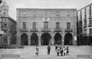 Perspectiva de la Plaça Major i la Casa de la Ciutat. Aquest majestuós edifici fou bastit entre els anys 1739 i 1777 sota les ordres del mestre d'obres Jeroni Torrents, per reemplaçar la casa del Consell de la Ciutat, que des del 1658 ocupava el mateix solar i que l'any 1713 havia estat incendiat. Durant molt de temps, a la planta principal es trobava el despatx de l'Alcaldia, les oficines i el Saló de Plens (inaugurat el 1885); i, a la segona planta, l'Arxiu, la Biblioteca i el Museu Municipal, serveis creats l'any 1896 sota l'alcaldia de Francesc Gallifa i Gomis. Avui dia, tot l'edifici és destinat a dependències municipals.
Procedència: Arxiu Jaume Pons i Agulló.