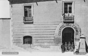 Detall de l'entrada de la casena del Carme l'any 1917. La caserna ocupava els terrenys on s'havia construït un convent de Carmelites al segle XIV. L'any 1835, arran de l'exclaustració monàstica, l'edifici fou cedit al municipi, que el destinà a escoles públiques, habilitades també com a col·legi electoral; més tard, esdevingué la seu d'allotjament de la tropa que des de la darrera carlinada va tenir una presència quasi constant a Manresa. Al tombant de segle, el recinte de la caserna va experimentar unes notables millores d'ampliació que hi van permetre la instal·lació de les oficines militars i de les quadres per a les cavalleries, les quals havien estat estatjades fins aleshores en cases particulars, amb les pertinents molèsties per als veïns. En la fotografia, els soldats pertanyents al batalló de caçadors de Reus fan guàrdia a l'entrada de la caserna.
Procedència: Arxiu Jaume Pons i Agulló.