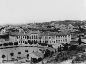 El Grup Escolar (l'actual Institut Lluís de Peguera). Al fons, es pot observar el barri del Poble Nou, l'antic escorxador i l'església de Sant Josep. Aquest enorme edifici educatiu que donà cabuda a l'Institut de Segon Ensenyament havia estat projectat l'any 1908 per commemorar el centenari de les batalles del Bruc. Però la seva construcció es va eternitzar per fases fins l'any 1927, data en què finalment s'inaugurà. Fidel Riu indicava que aquell any la plaça de l'Institut només servia com a camp d'esports, i es preguntava «perquè l'Ajuntament no es preocupa de fer d'allò un jardí públic, amb bancs de pedra i arbres frondosos que servissin d'ombradiu als vells i a la mainada? Enllestides les obres del passeig fóra, aquella una millora indicadíssima» .
Procedència: Arxiu Jaume Pons i Agulló.