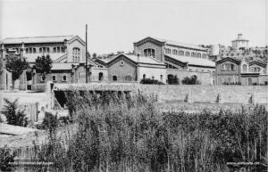 Panoràmica de l'Escorxador Municipal que fou traslladat de la seva primitiva ubicació, al final del carrer de les Piques, a uns terrenys situats al camí de Joncadella, on reuniria unes millors condicions de salubritat. Aquest monumental edifici públic va ser dissenyat per l'arquitecte Ignasi Oms i Ponsa, i aixecat entre el 1906 i el 1908, sota l'alcaldia de Pere Armengou i Manso. La fotografia va ser feta probablement durant el primer decenni del segle XX. Al fons la casa Viñas, construïda durant el primer quart de segle XX sobre el tossal de la Talaia.
Procedència: Arxiu Josep Miravitlles