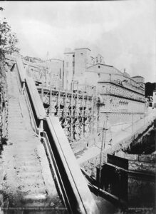 Fotografia de les obres de construcció de la nova casa de tercera provació (l'actual Casa d'Exercicis). Les obres s'iniciaren el 27 de juliol de 1894 i van ser finançades per Dolors Serra i de Chopitea, vídua de Pons. El nou edifici estableix una connexió interior perfecta amb la Cova -a través de la sagristia- i amb la Casa antiga. En les obres de l'actual Casa d'Exercicis treballaren ininterrompudament uns 140 obrers, de tal manera que la construcció fou molt ràpida. La benedicció del nou edifici es va dur a terme el 21 de setembre de 1896, en una senzilla cerimònia de caràcter religiós, sense que les autoritats municipals hi fossin presents.
Procedència: Arxiu Històric de la Companyia de Jesús de Catalunya.